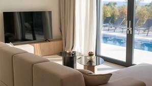 Un saló modern amb un sofà, una taula de centre de vidre, una televisió de pantalla plana i vista a una piscina i zona d'estar a l'aire lliure.