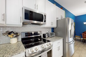 A kitchen with white cabinets, a stainless steel microwave, a stove, and a refrigerator. - Dog-friendly home with private pool, yoga studio, fitness room & great patio (Sun City)