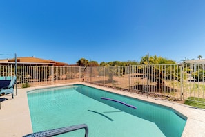 A swimming pool with a white fence, a lounge chair, and a palm tree in the background. - Dog-friendly home with private pool, yoga studio, fitness room & great patio (Sun City)