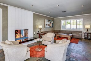 A modern living room with a fireplace, comfortable seating, and a large window. - Classic Palm Springs Retreat with Mountain-View Pool (Palm Springs)