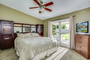 Ein Schlafzimmer mit einem großen Bett, einem Deckenventilator, einem Fernseher, einer hölzernen Kommode und einer Glastür zum Balkon.