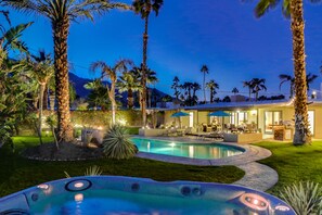 Ein Poolbereich mit Whirlpool, umgeben von Palmen und einer gut beleuchteten Außenlounge.