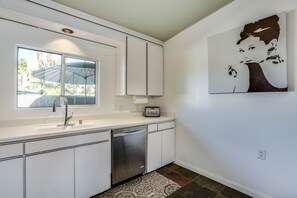 Cocina moderna con armarios blancos, lavavajillas de acero inoxidable, una ventana con un paraguas y un cuadro colgado en la pared.