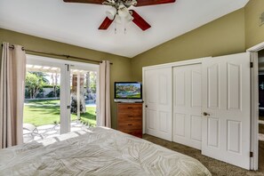 Un dormitorio con una cama, un televisor sobre una cómoda y un ventanal corredizo que da a un jardín.