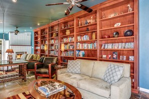 Amplia sala de estar con una gran estantería de madera llena de libros y objetos decorativos, un sofá cómodo y una mesa de centro con libros.