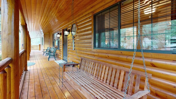 Una baita di legno con un portico, una panchina e due sedie.
