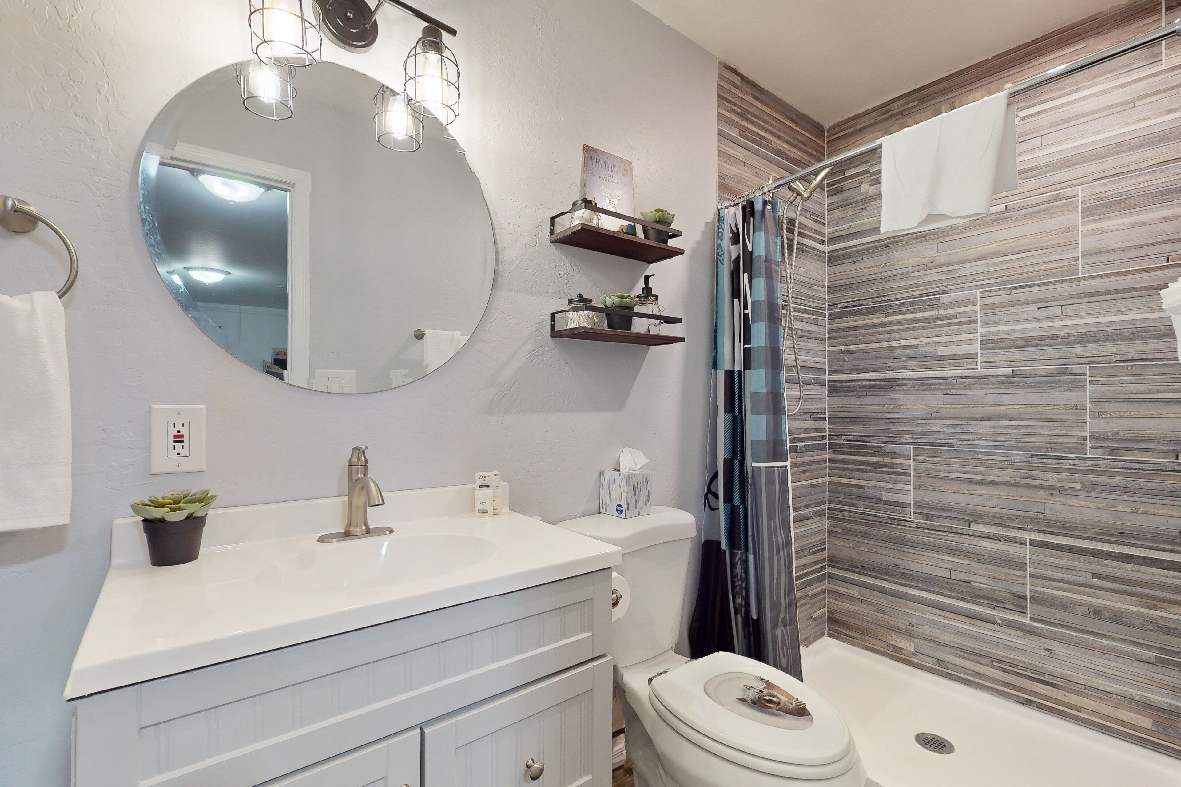 A bathroom with a white vanity, a round mirror, a toilet, and a shower with a striped curtain.