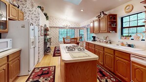 Una cucina con mobili in legno, un frigorifero bianco, un forno a microonde, un fornello e un lavandino. Gli scaffali sono decorati e c'è una finestra con vista sugli alberi.