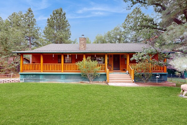 A log cabin with a porch, surrounded by a well-maintained lawn and trees. - Two-story home with game room, large deck, bbq grill, & yard (Lakeside)