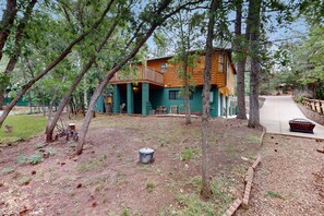 A rustic cabin with a wooden exterior, surrounded by trees and a paved pathway. - Two-story home with game room, large deck, bbq grill, & yard (Lakeside)