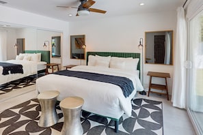 Une chambre d’hôtel moderne avec un grand lit, deux tables de chevet, un ventilateur de plafond et un grand miroir.
