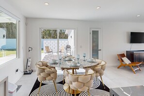 A modern dining area with a round table set for six, a television mounted on the wall, and a view of the outdoor patio. - Beautiful home with private pool, pool spa & open living space (Palm Springs)