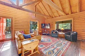 A log cabin interior with a leather sofa, a patterned rug, a television, and a fireplace. - Dog-friendly cabin in the woods with WiFi, wood stove, and private washer/dryer (Idyllwild)