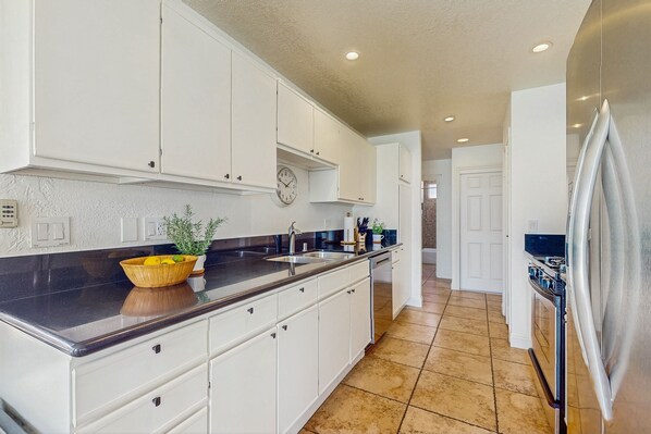 A kitchen with white cabinets, a black countertop, a stainless steel refrigerator, and a clock on the wall. - Jewel on a double lot with a private pool, spa, and resort like yard (La Quinta)