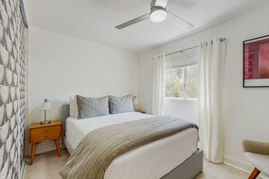 A bedroom with a bed, a nightstand, a ceiling fan, a window with curtains, and a chair. - Jewel on a double lot with a private pool, spa, and resort like yard (La Quinta)