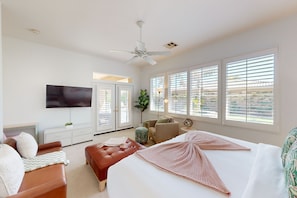 A modern bedroom with a large bed, a TV, a ceiling fan, and large windows with blinds. - Palm Desert retreat with private pool, fireplace, & W/D & Pet Friendly (Palm Desert)