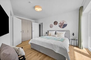 A modern bedroom with a bed, a side table, a wall-mounted light, and a door. - The View B02 Achter de Diek - beach chair, elevator, shared Sauna (Dagebüll)
