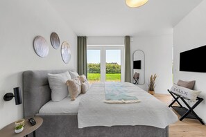 Ein modernes Schlafzimmer mit einem großen Bett, einem Flachbildfernseher und Blick auf Grünflächen.