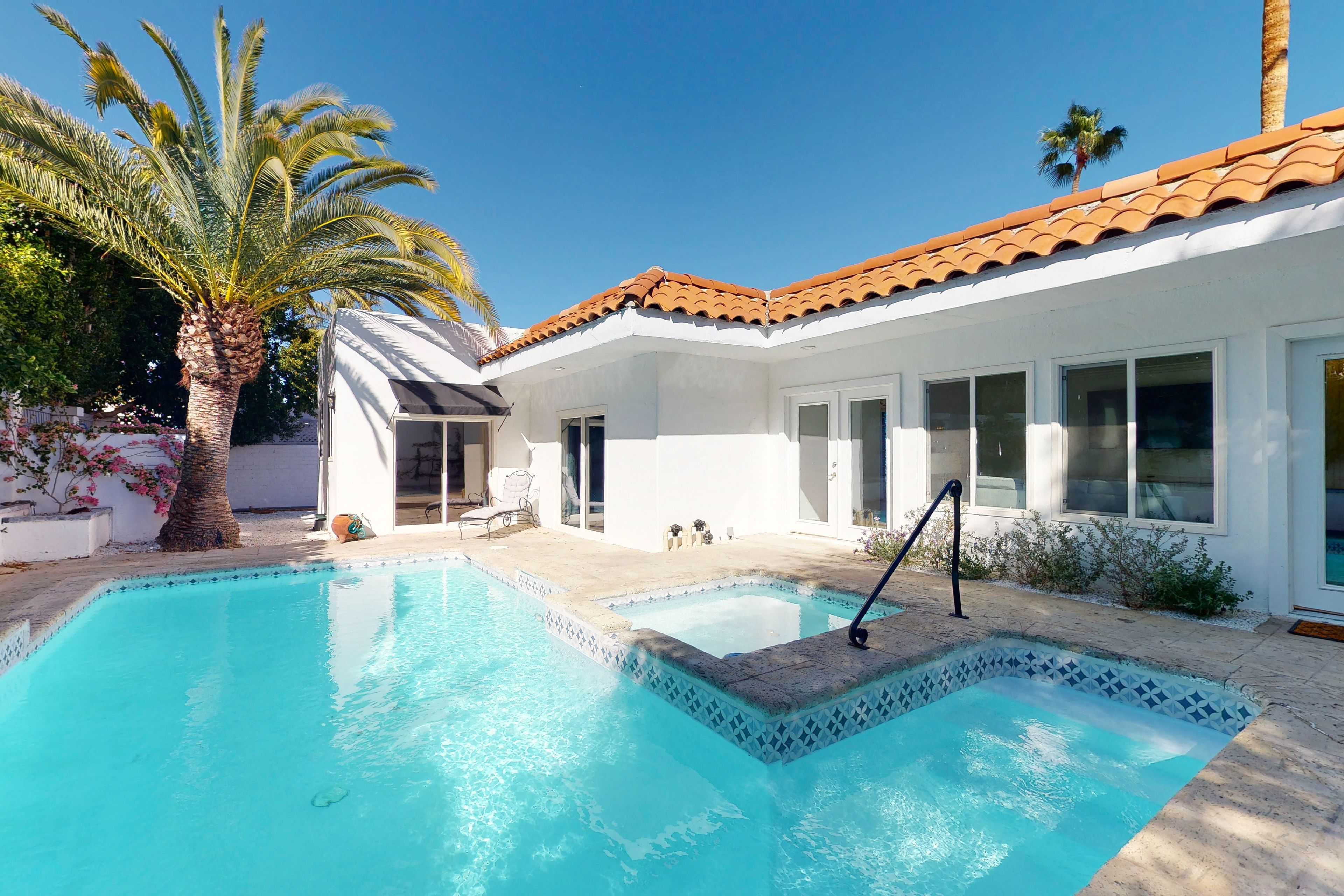 A pool with a tiled border, a palm tree, and a building with a tiled roof.