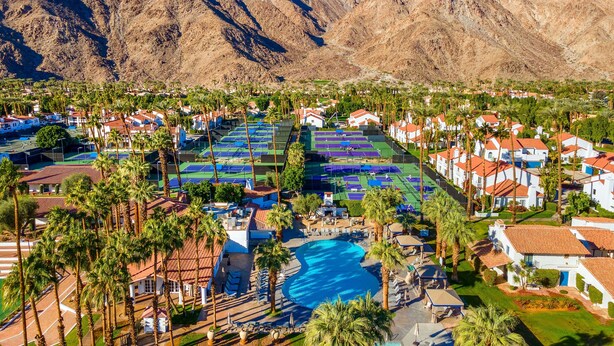 Un resort con una gran piscina, varias canchas de tenis y montañas al fondo.