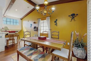A dining area with a wooden table, chairs, and a bench. There is a chandelier above the table, and a window with curtains to the left. - Palm-lined mountain view condo with heated pool, tennis, grill, fireplace, & AC (La Quinta)