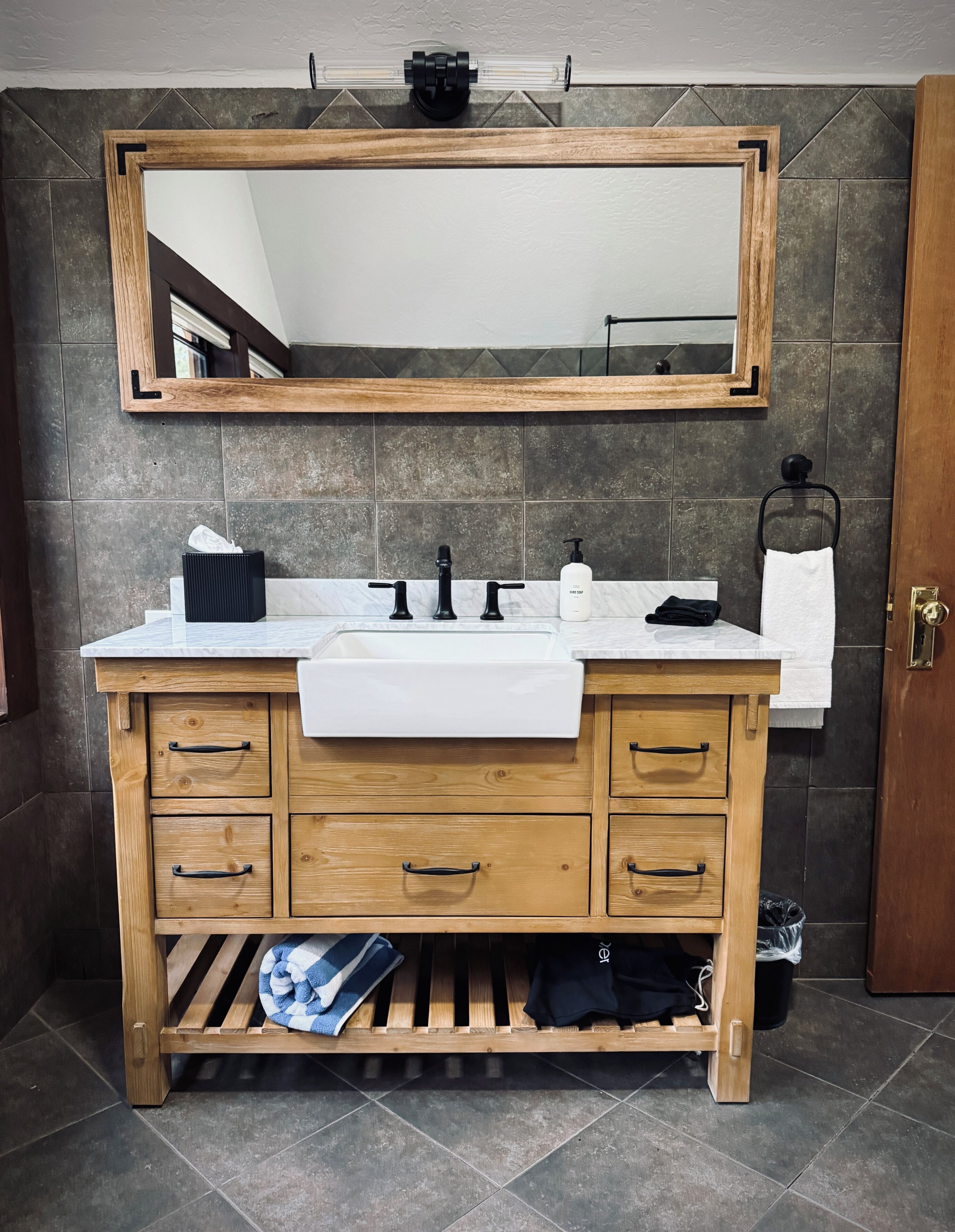 A wooden vanity with a white sink, three black faucets, a mirror above, and a towel rack to the right.