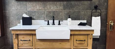 A wooden vanity with a white sink, three black faucets, a mirror above, and a towel rack to the right.