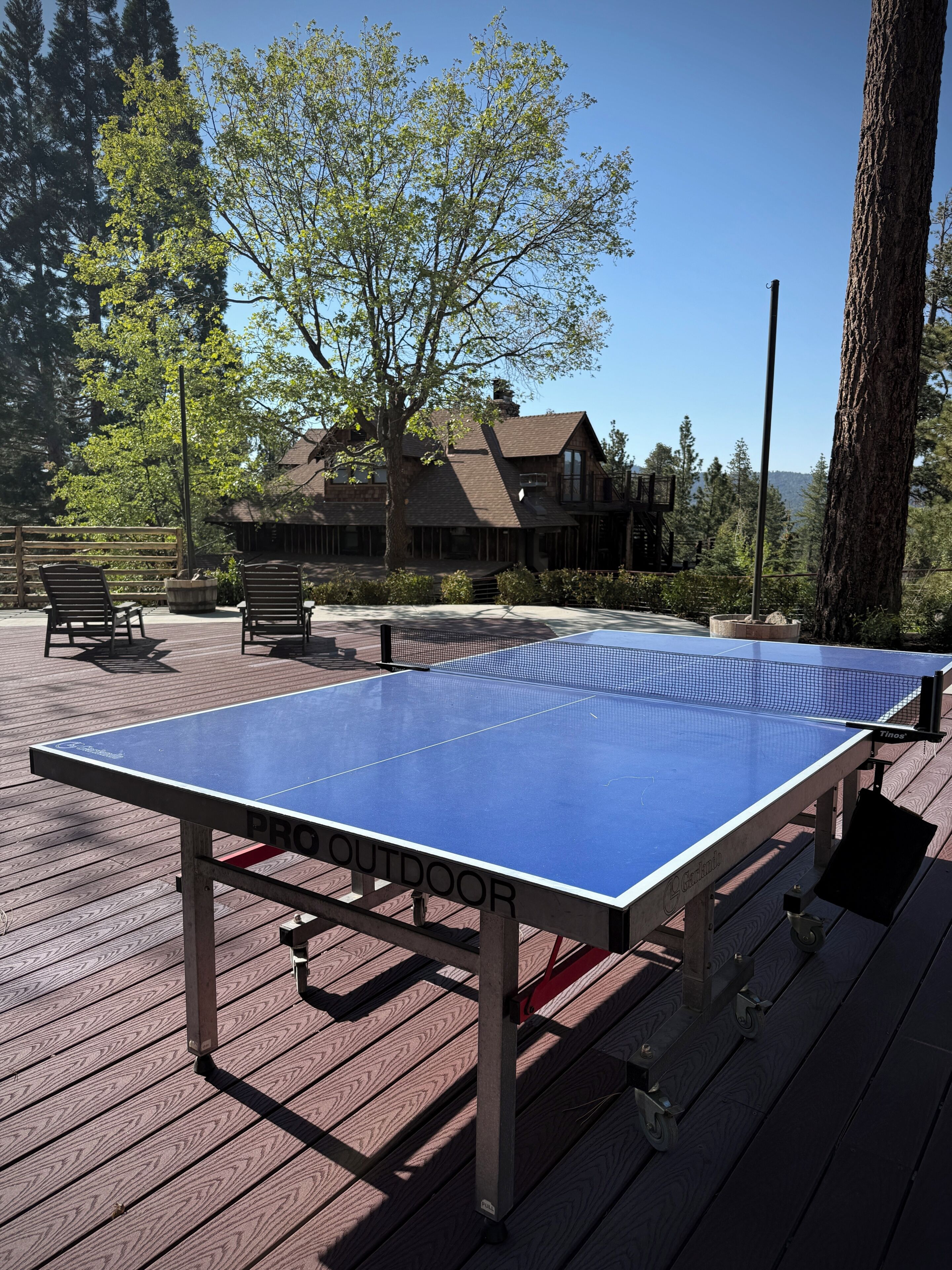 Una mesa de ping pong en una terraza de madera con una casa al fondo.