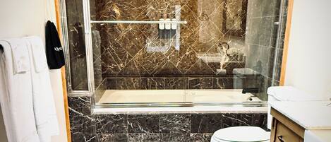 A bathroom with a glass-enclosed shower, a toilet, and a vanity with drawers.