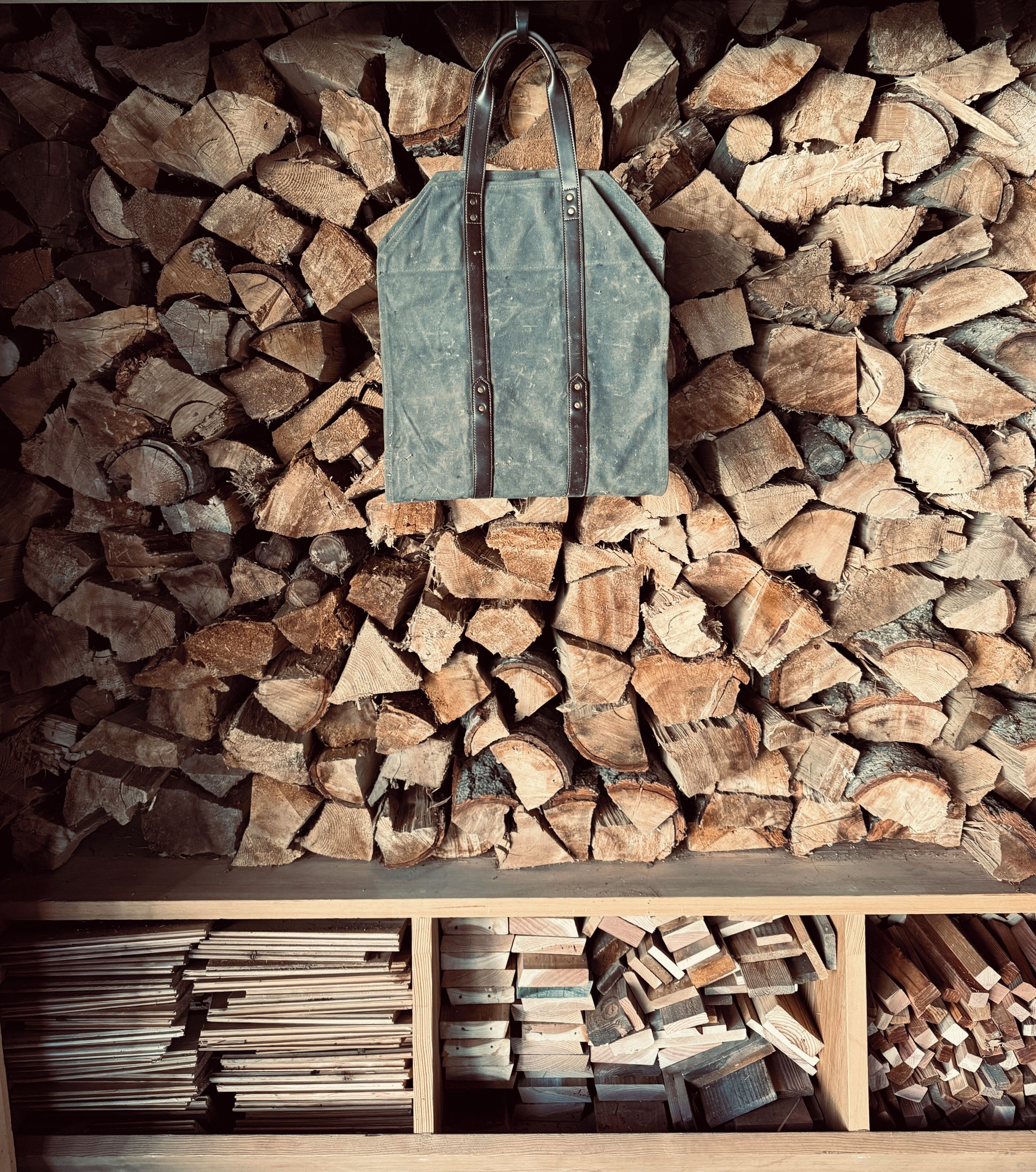 A wooden bench with a bag hanging on a strap above it, set against a backdrop of stacked firewood.