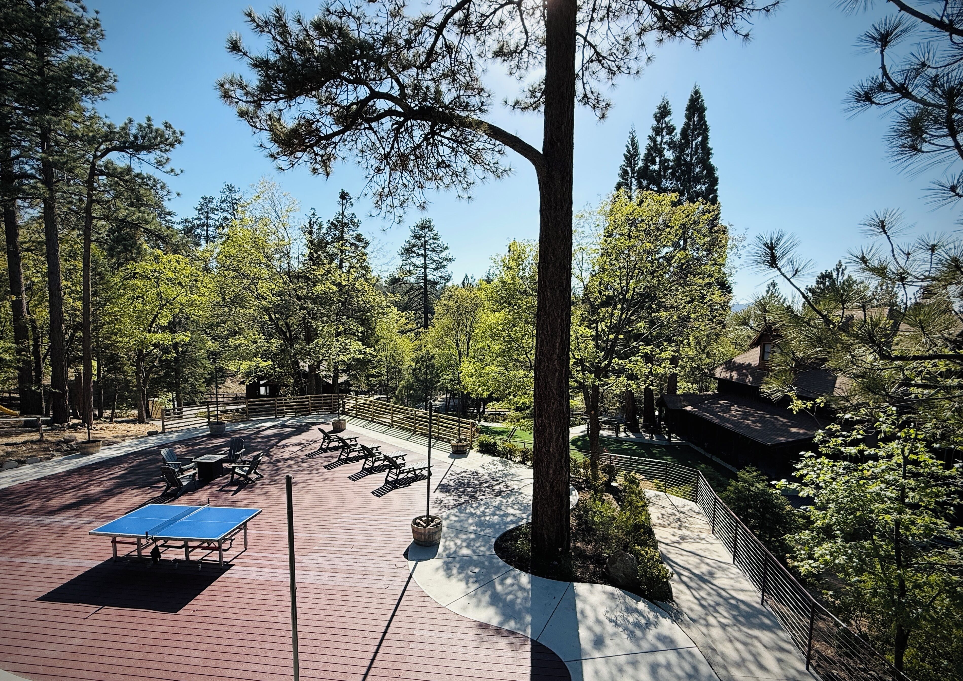 A park with picnic tables, a ping pong table, and a building with a sloped roof.