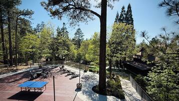 A park with picnic tables, a ping pong table, and a building with a sloped roof.