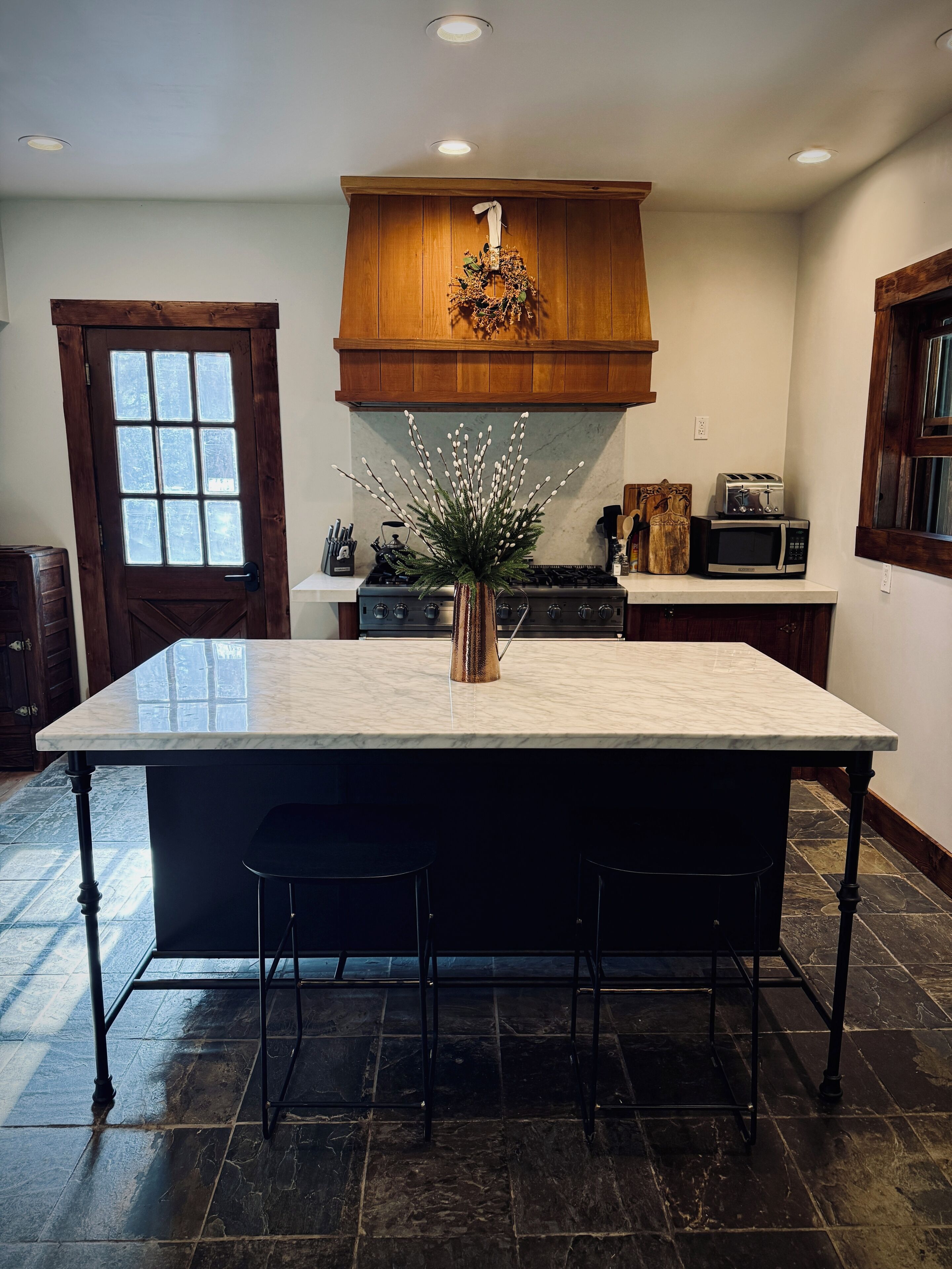 A kitchen with a large island, wooden cabinets, a microwave, and a decorative wreath.