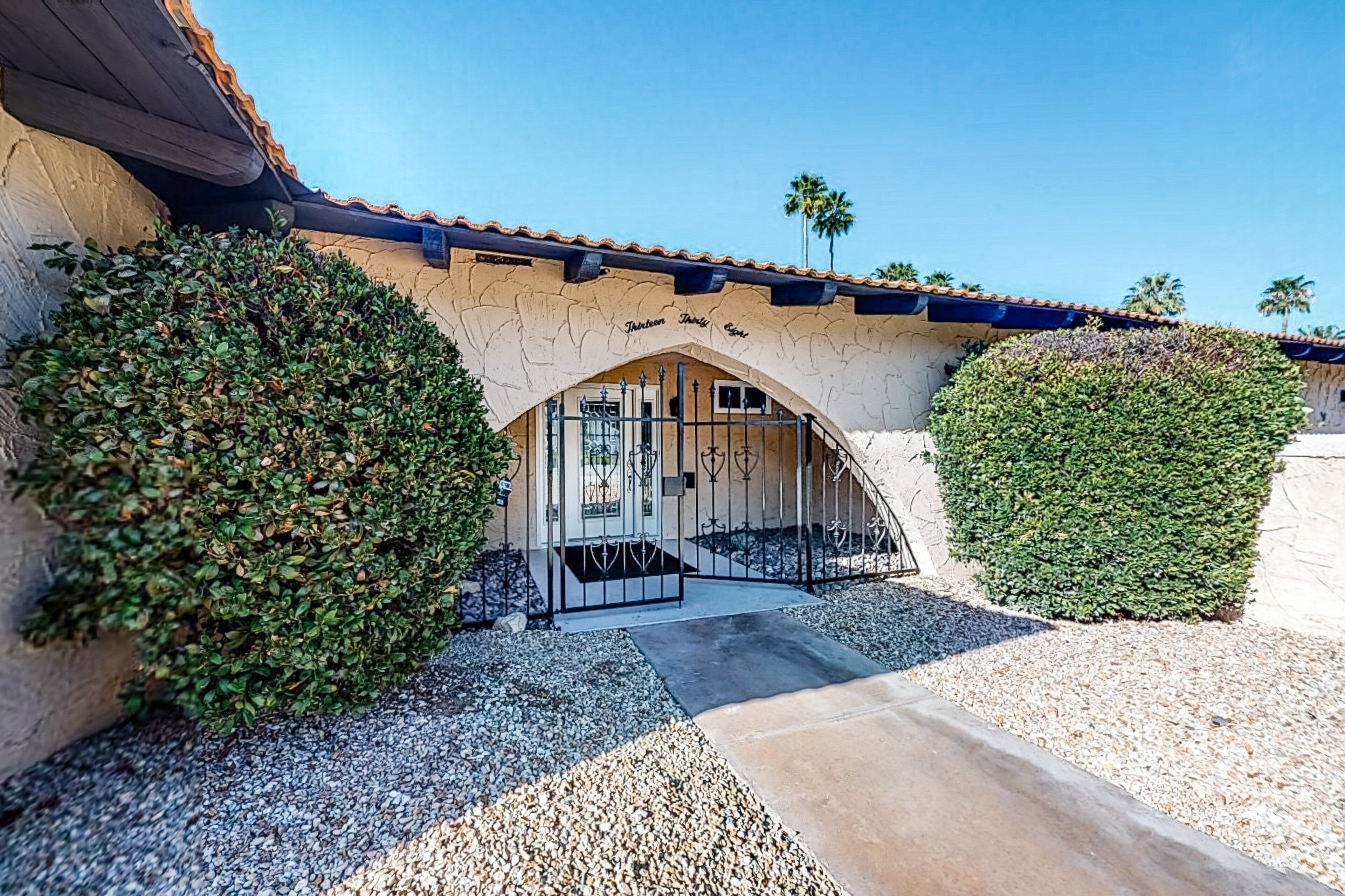 A building entrance with a covered walkway, a stone wall, and a palm tree in the background.