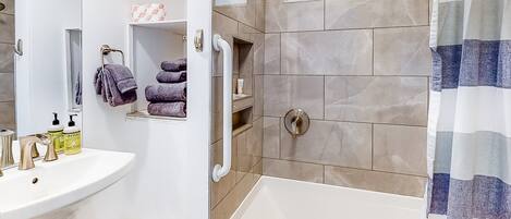 A bathroom with a white sink, a bathtub, and a shower area. There are towels and toiletries on the sink.
