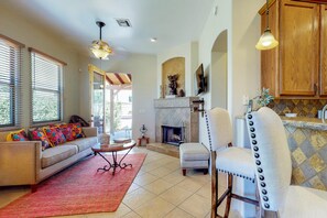Una sala de estar con sofá, sillón, chimenea y comedor con mesa y sillas.