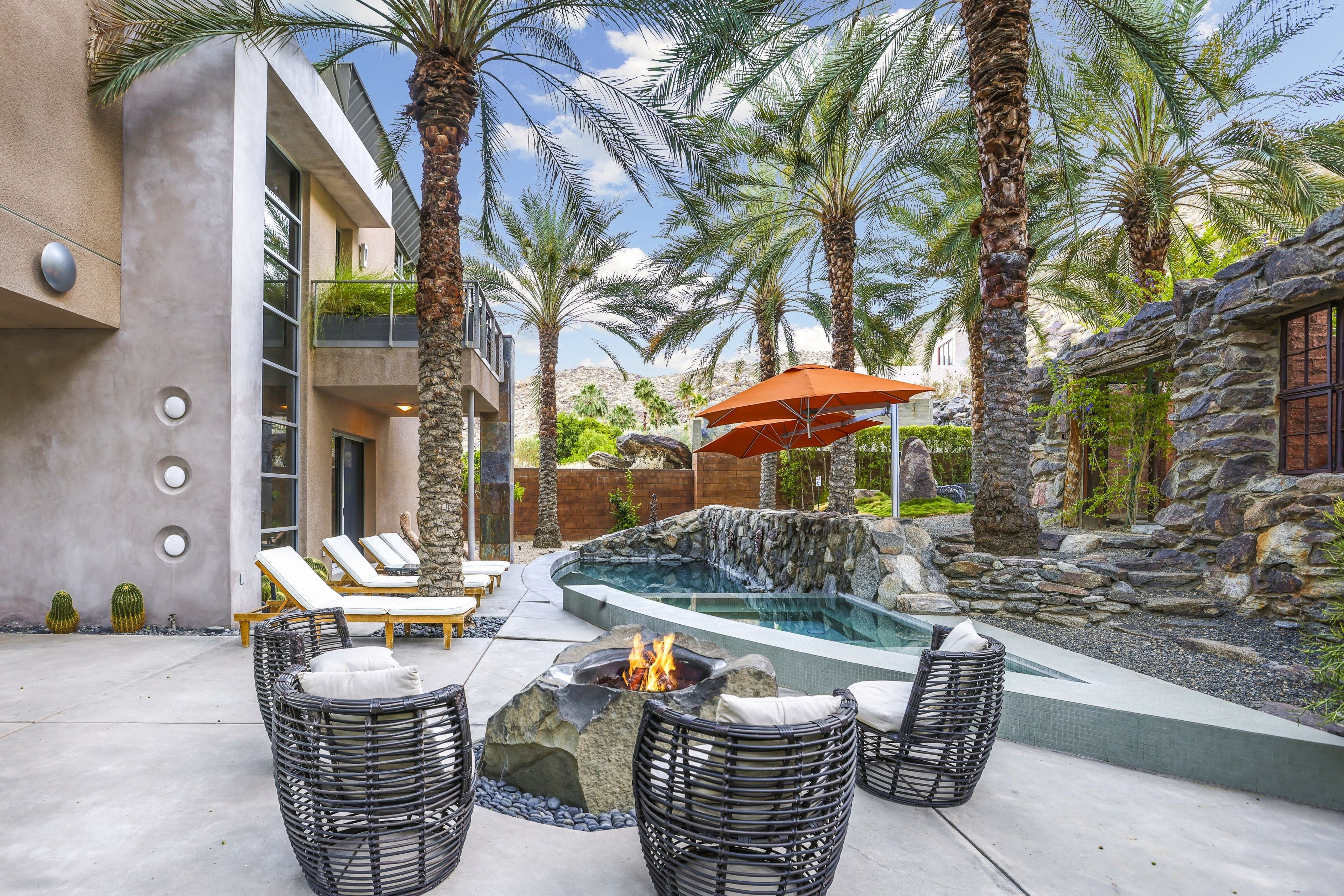 A modern outdoor pool area with lounge chairs, a fire pit, and a stone wall.