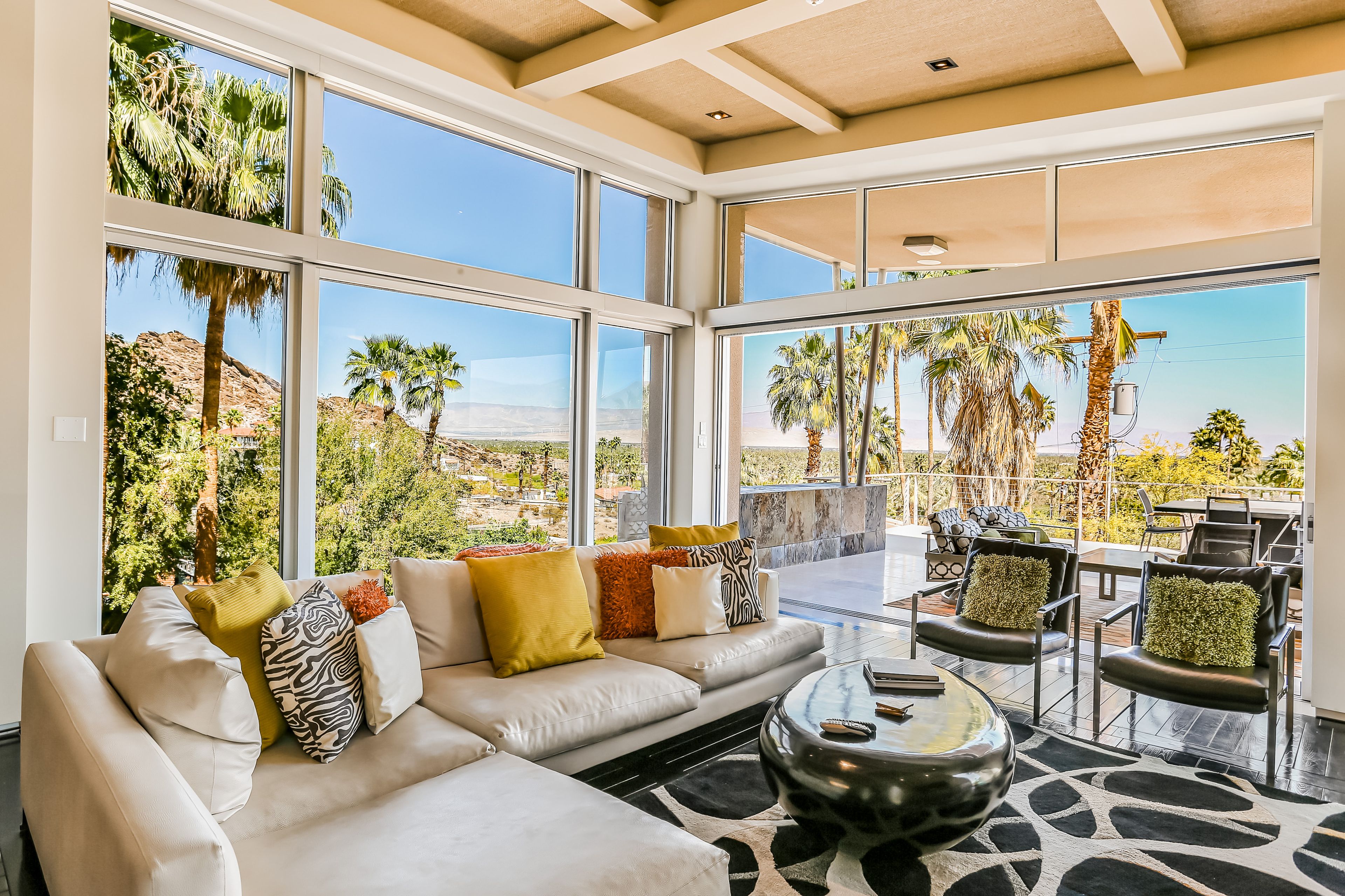 A spacious living area with a large window overlooking a scenic landscape, a comfortable sofa with various cushions, and a dining area with chairs and a table.