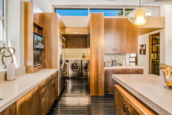 A modern kitchen with wooden cabinets, a built-in washing machine, and a large window. - One-of-a-kind luxury home with private pool & spa, WiFi, AC & on-site ruins (Palm Springs)