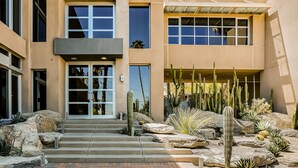 Un bâtiment moderne doté d’une entrée en verre, d’un escalier en pierre et d’un jardin désertique planté de cactus.