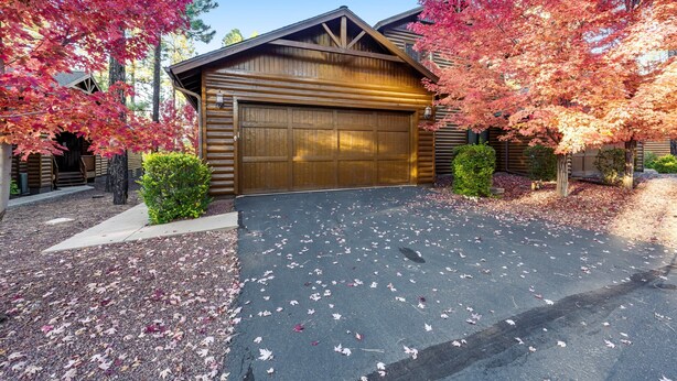 A wooden cabin with a garage, surrounded by trees with autumn leaves. - Hideaway in the pines with pool table, covered deck, fireplace, grill, & W/D (Pinetop)