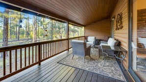 A covered porch with a wooden railing, wicker furniture, and a view of a forest. - Hideaway in the pines with pool table, covered deck, fireplace, grill, & W/D (Pinetop)