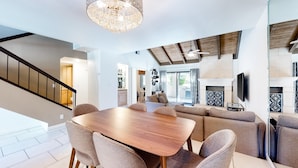 Una sala de estar moderna con una mesa de comedor de madera, sofás color beige y una araña.