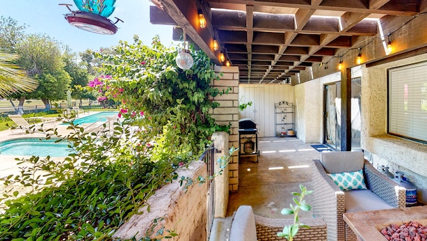 Un patio exterior techado con piscina, zona de estar y una parrilla.