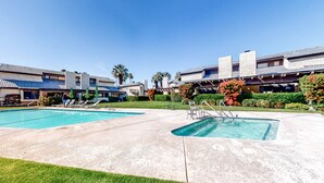 Zona de piscina con dos piscinas, sillas de descanso y un porche cubierto.