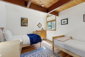 Un dormitorio con dos camas, un aparador de madera, un escritorio y una ventana con vista a árboles.