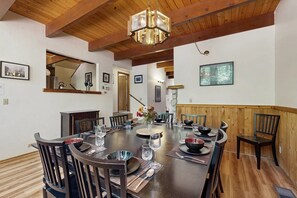 Un coin repas avec une table en bois dressée pour six personnes, entourée de chaises, avec un plafond en bois et un luminaire suspendu.