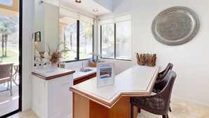 Cozinha moderna com uma ilha grande, área de refeições com cadeiras de vime e um painel decorativo de metal na parede.