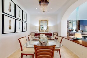 A dining area with a glass table, wooden chairs, and framed artwork on the wall. - Lavish condo on 14th tee of Arnold Palmer course at PGA West (La Quinta)