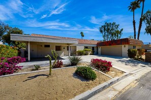 A two-story house with a tiled roof, surrounded by landscaped gardens and palm trees. - Ground-floor, golf-adjacent getaway w/ free WiFi, central A/C, & 20 shared pools (Palm Desert)